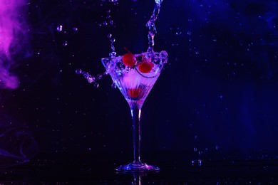 Photo of Pouring fresh martini into glass on table in neon lights