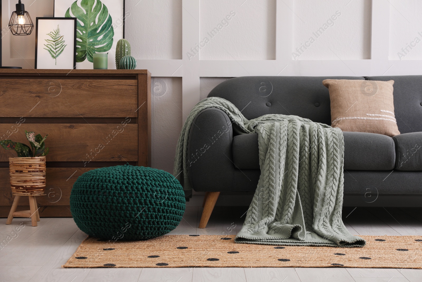 Photo of Stylish living room interior with knitted pouf, sofa and wooden chest of drawers