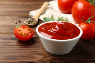 Photo of Delicious ketchup in bowl and tomatoes on wooden table, closeup