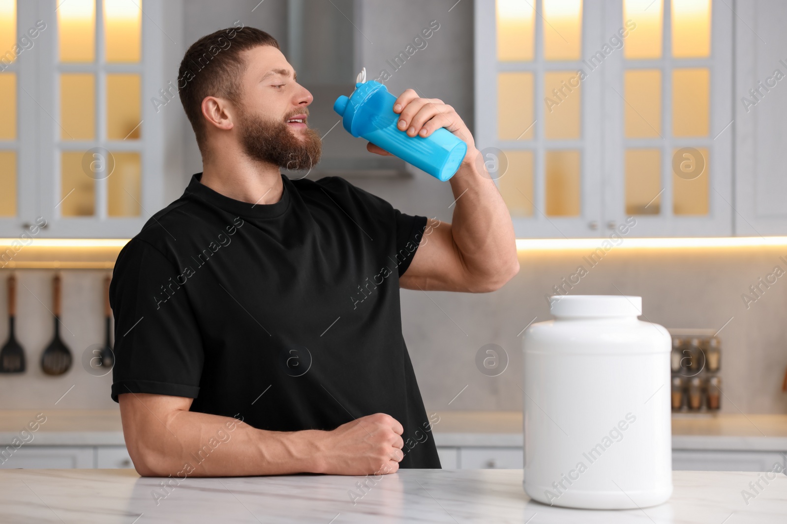 Photo of Young man with shaker of protein and powder at white marble table in kitchen