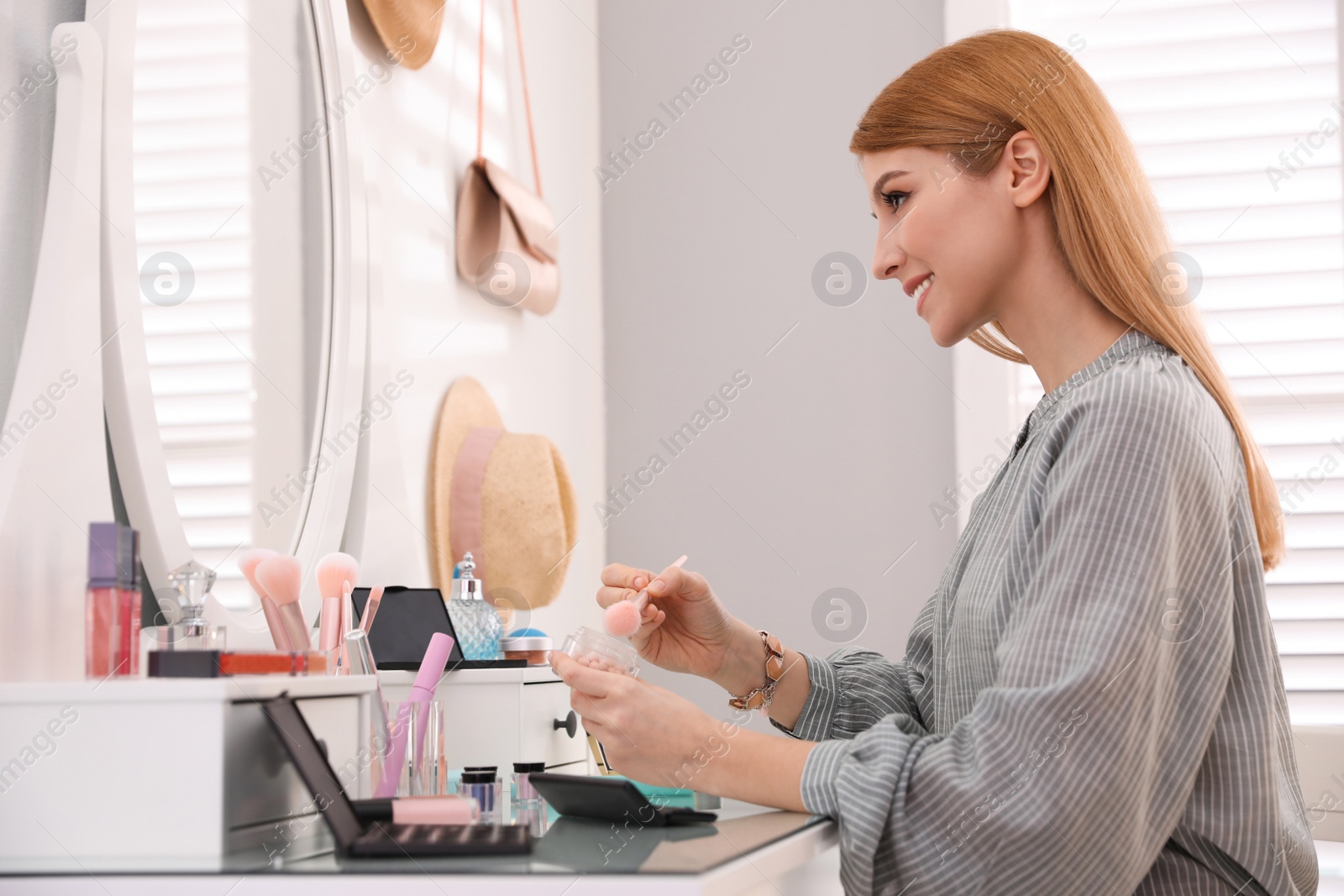 Photo of Beautiful young woman applying makeup near mirror in dressing room