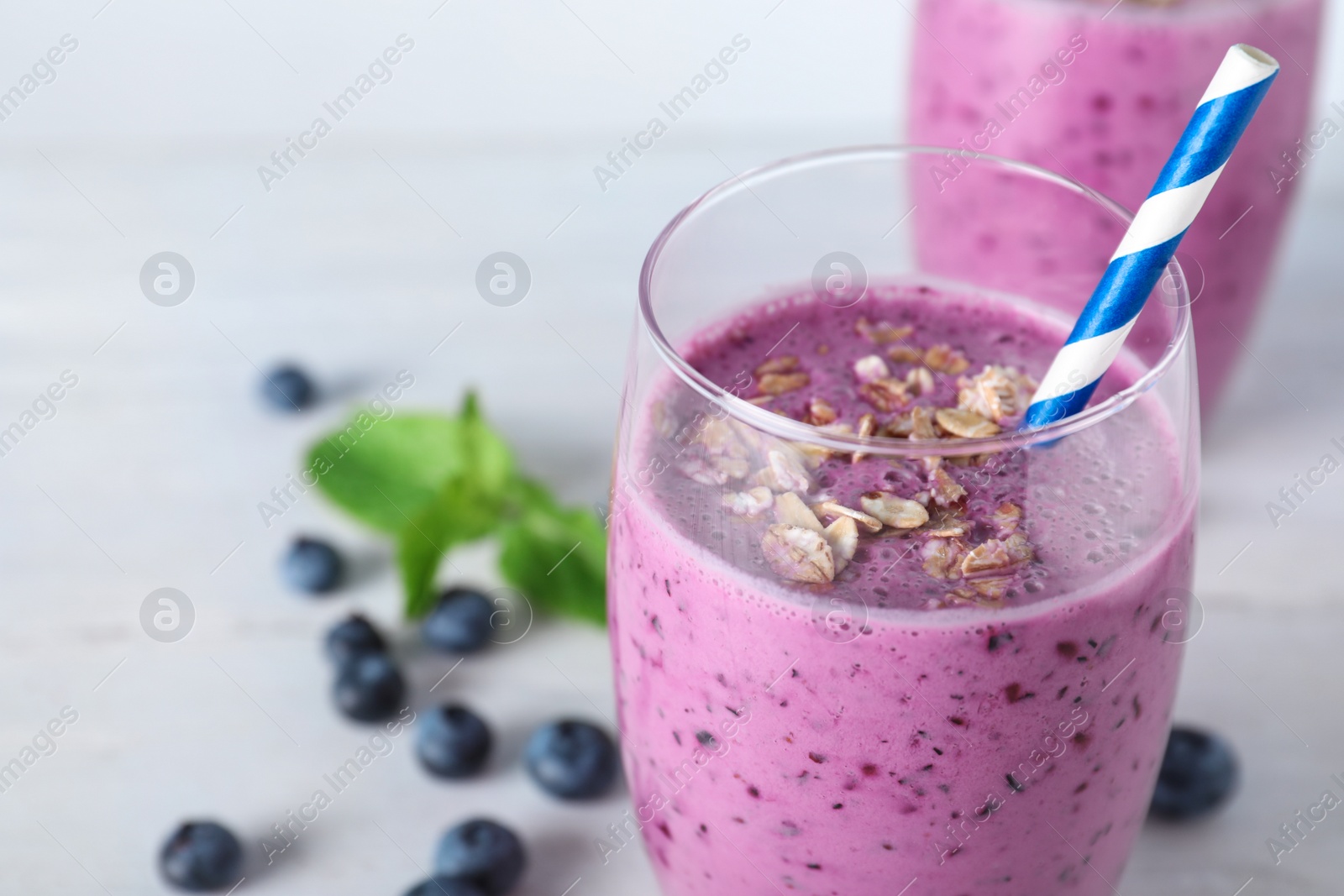 Photo of Glass of tasty blueberry smoothie with straw on white table, closeup