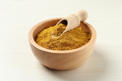 Photo of Dry curry powder in bowl and scoop on light wooden table, closeup