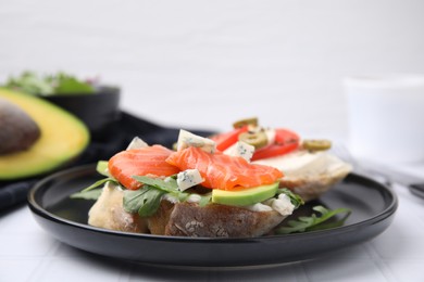 Photo of Plate with different tasty bruschettas on white tiled table, closeup