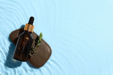 Bottle of cosmetic oil, leaves and stone in water on light blue background, top view. Space for text