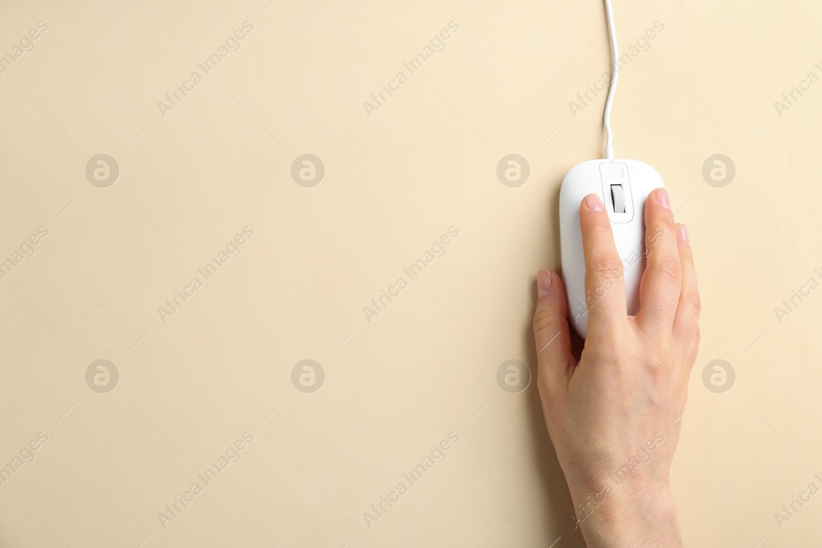 Photo of Woman using modern wired optical mouse on beige background, top view. Space for text