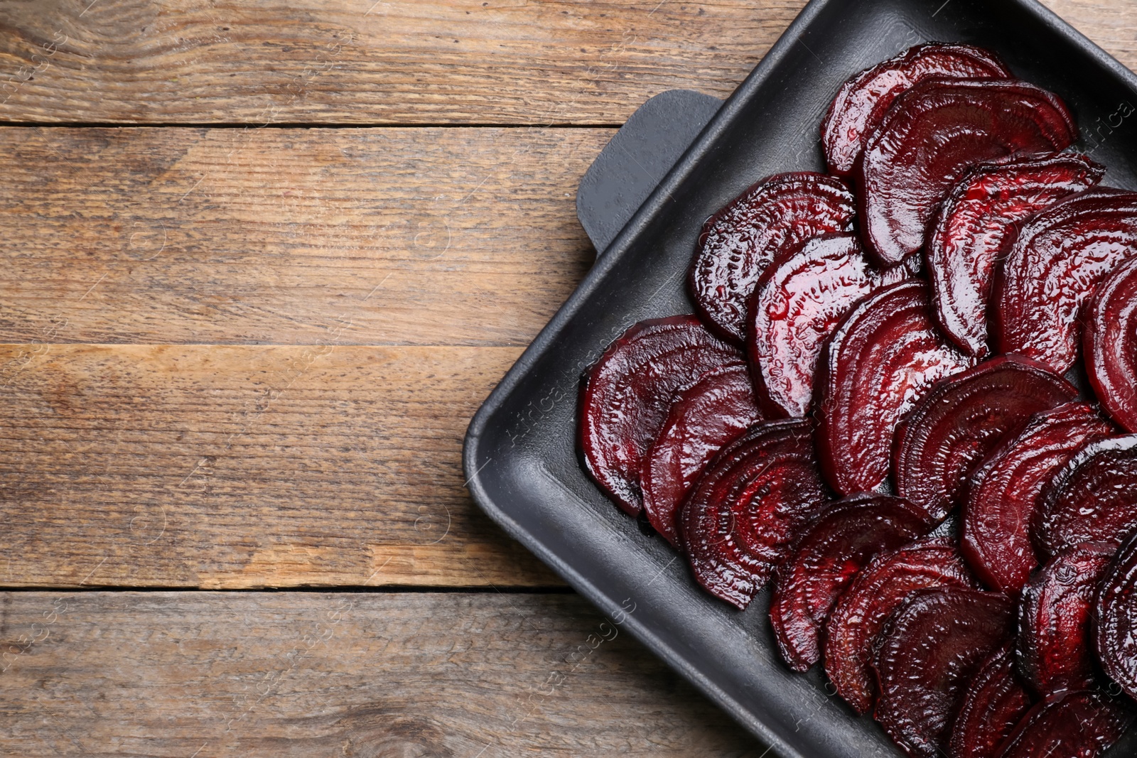 Photo of Baking dish with roasted beetroot slices on wooden table, top view. Space for text