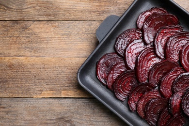 Baking dish with roasted beetroot slices on wooden table, top view. Space for text