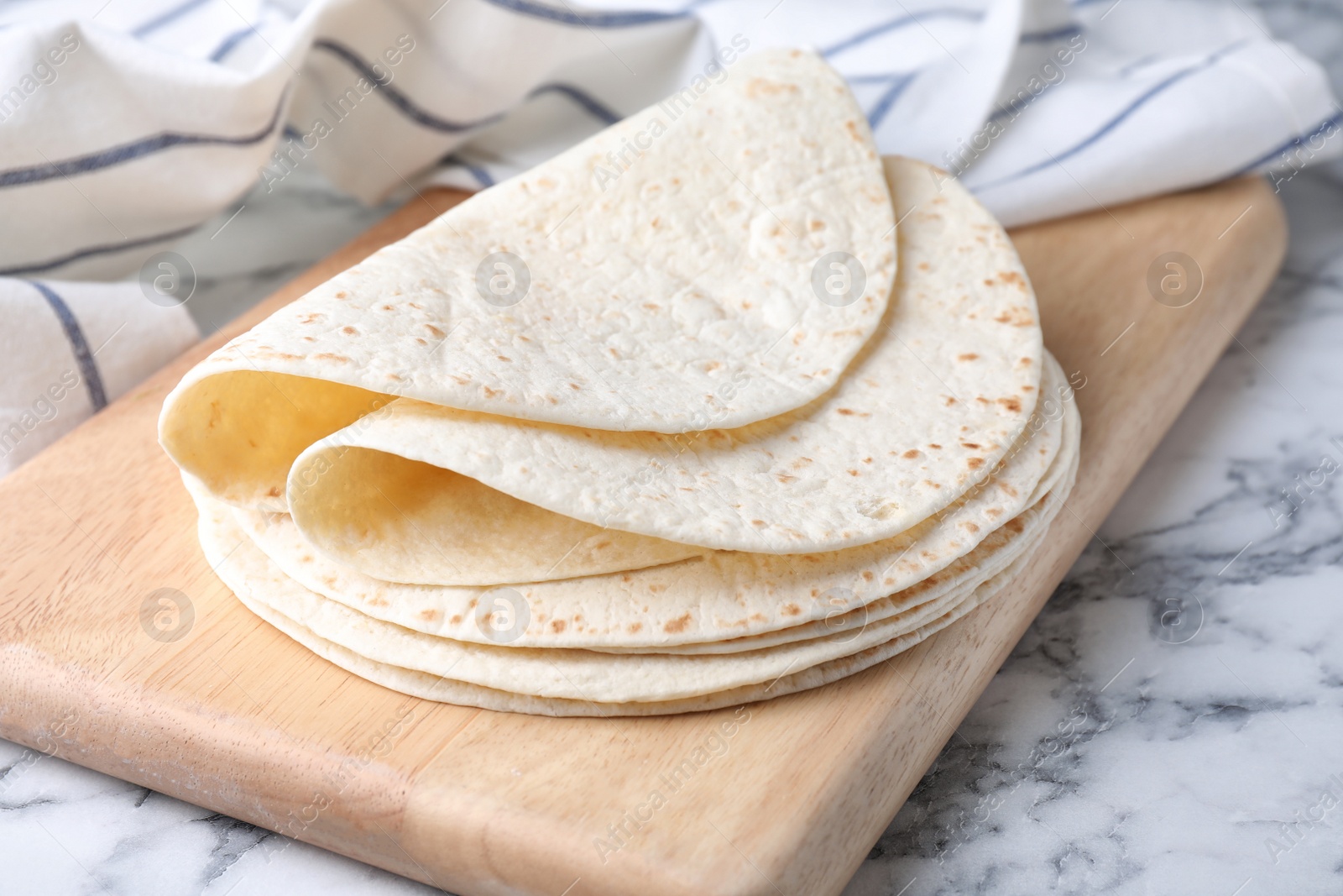 Photo of Wooden board with corn tortillas on marble table. Unleavened bread
