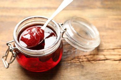 Photo of Delicious pickled strawberry jam in glass jar on wooden table, closeup
