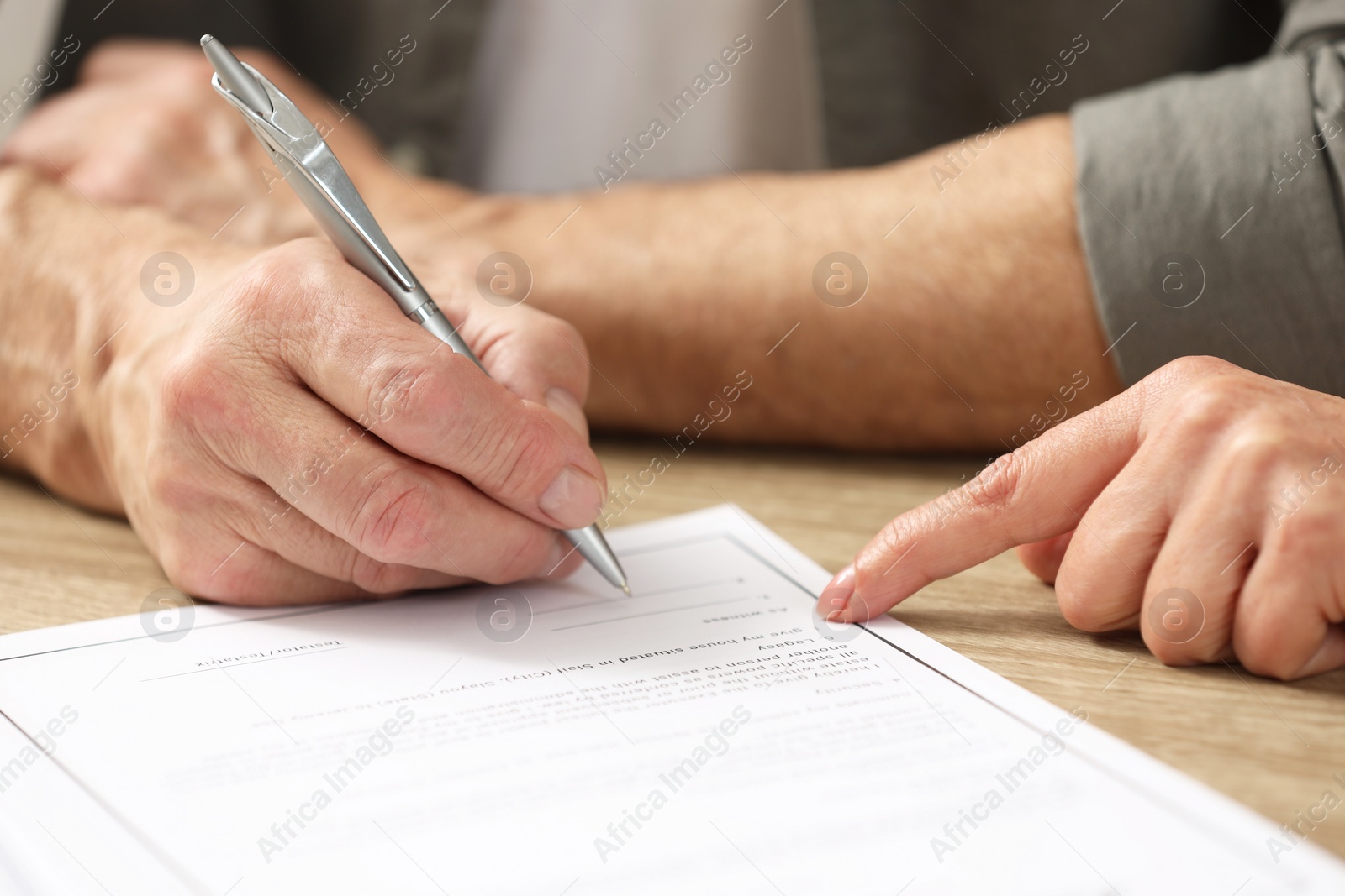 Photo of Notary pointing to senior man where to sign Last Will and Testament at wooden table, closeup