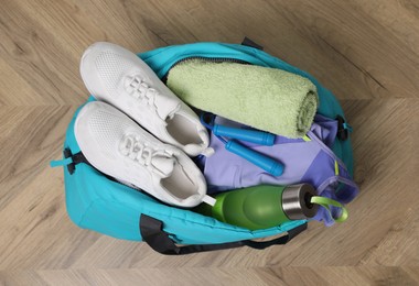 Blue gym bag with sports accessories on wooden floor, top view