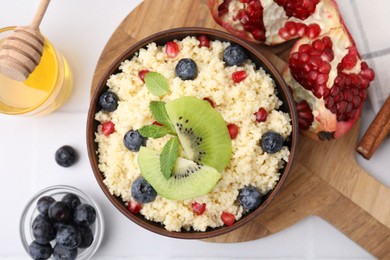 Photo of Bowl of tasty couscous with kiwi, blueberries, pomegranate and honey on white table, flat lay