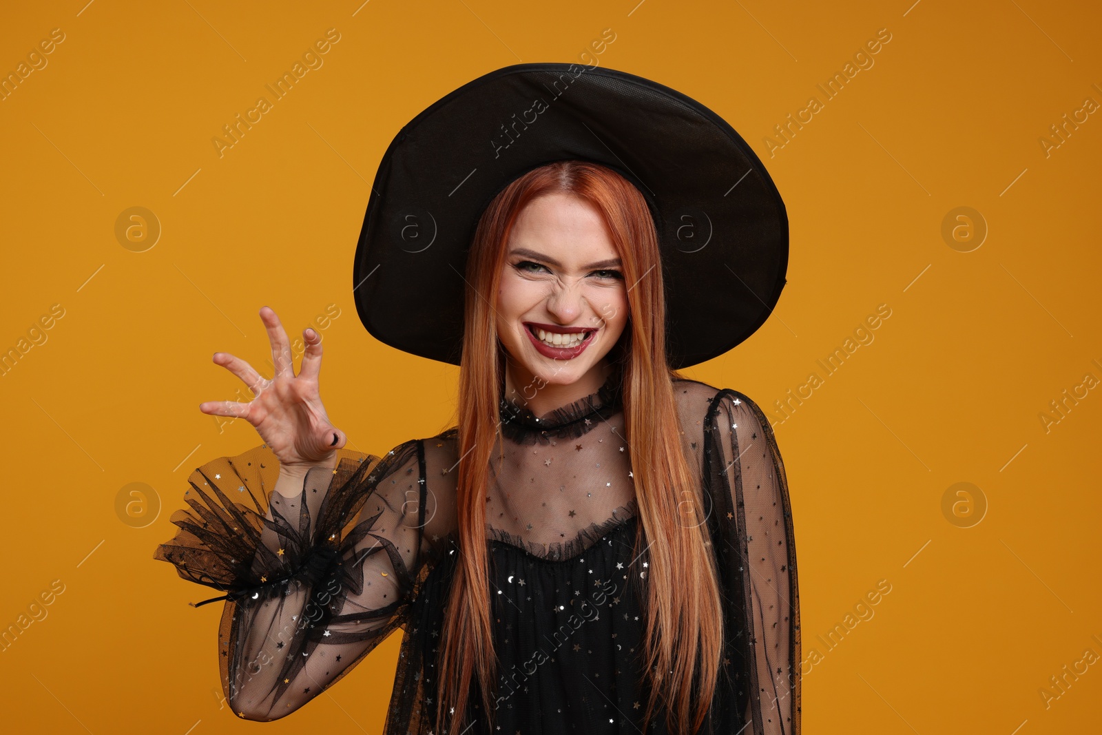 Photo of Young woman in scary witch costume on orange background. Halloween celebration