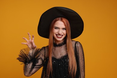 Young woman in scary witch costume on orange background. Halloween celebration