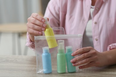 Photo of Woman packing cosmetic travel kit at wooden table indoors, closeup. Bath accessories