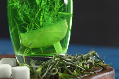 Glass of homemade refreshing tarragon drink, sprigs and sugar cubes on wooden board, closeup