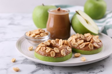 Photo of Fresh green apples with peanut butter and nuts on white marble table, closeup