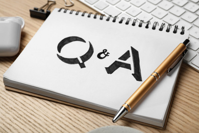 Photo of Notebook with text Q&A and pen on wooden table, closeup