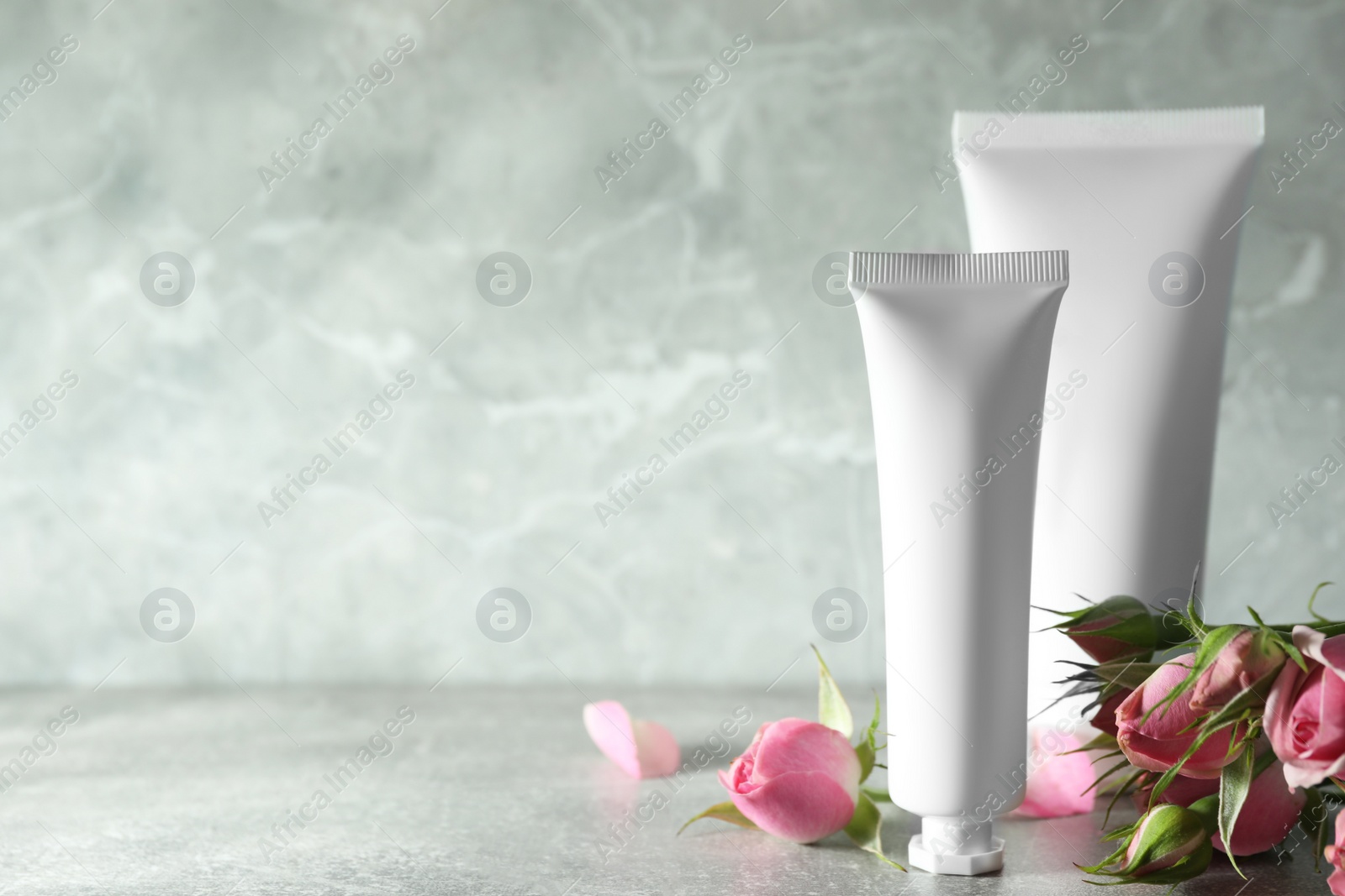 Photo of Tubes of hand cream and beautiful roses on light grey table, space for text