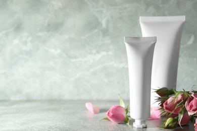 Photo of Tubes of hand cream and beautiful roses on light grey table, space for text