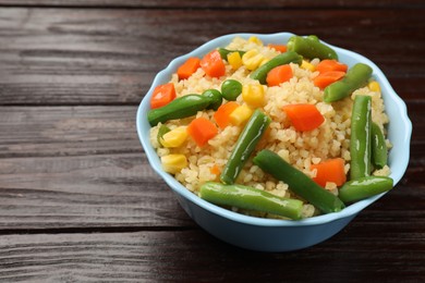 Photo of Delicious bulgur with vegetables in bowl on wooden table, closeup. Space for text