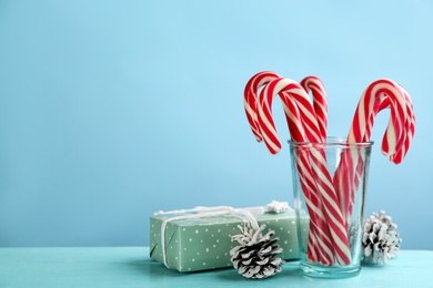 Photo of Many sweet candy canes in glass, gift box and Christmas decor on light blue wooden table. Space for text