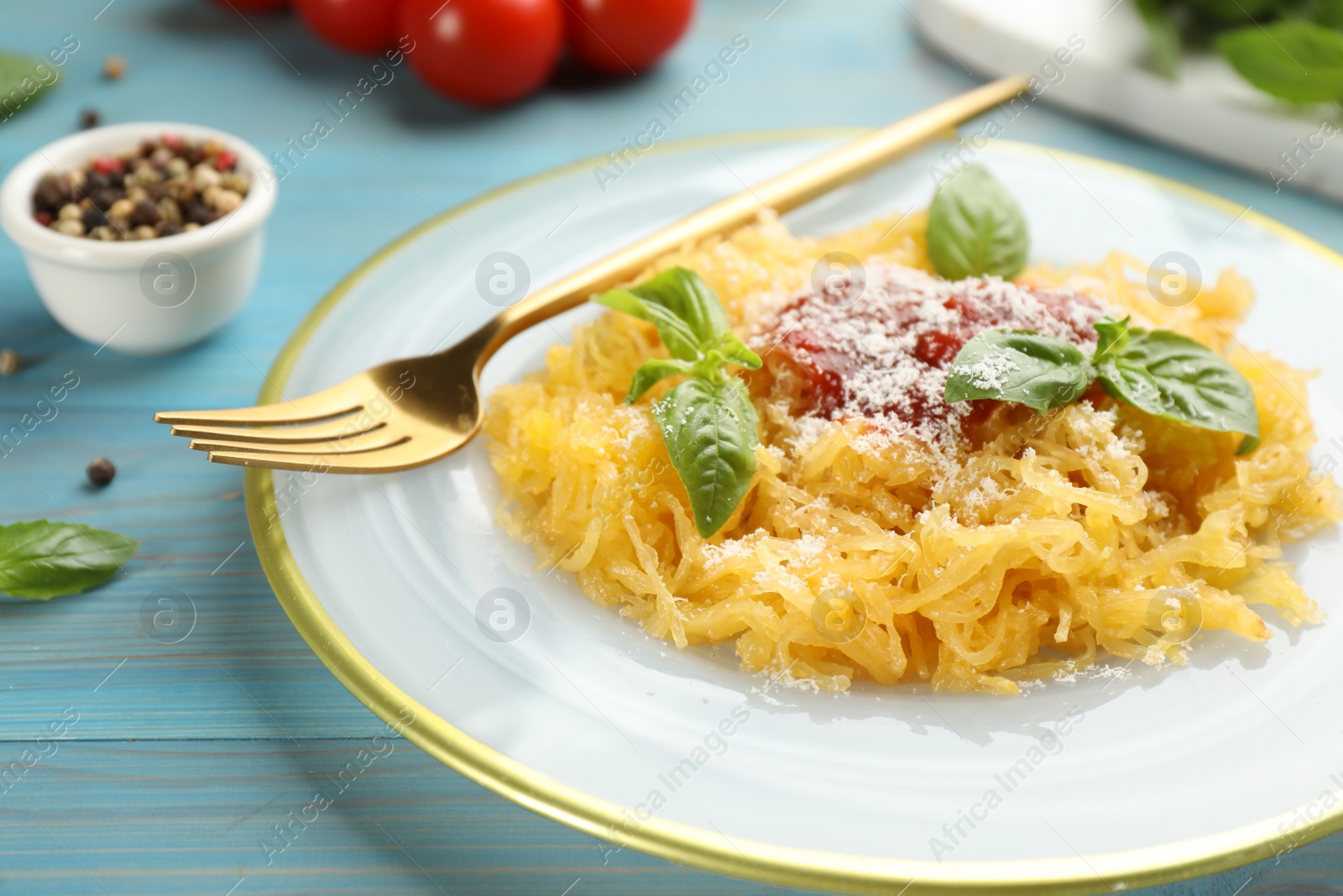 Photo of Tasty spaghetti squash with tomato sauce, cheese and basil served on light blue wooden table, closeup