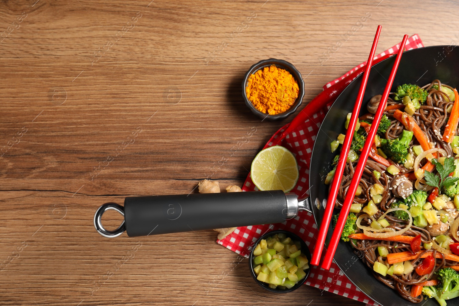 Photo of Stir-fry. Tasty noodles with meat in wok, chopsticks and ingredients on wooden table, flat lay. Space for text