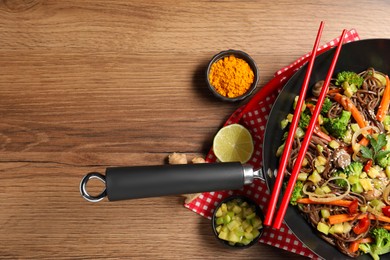 Photo of Stir-fry. Tasty noodles with meat in wok, chopsticks and ingredients on wooden table, flat lay. Space for text