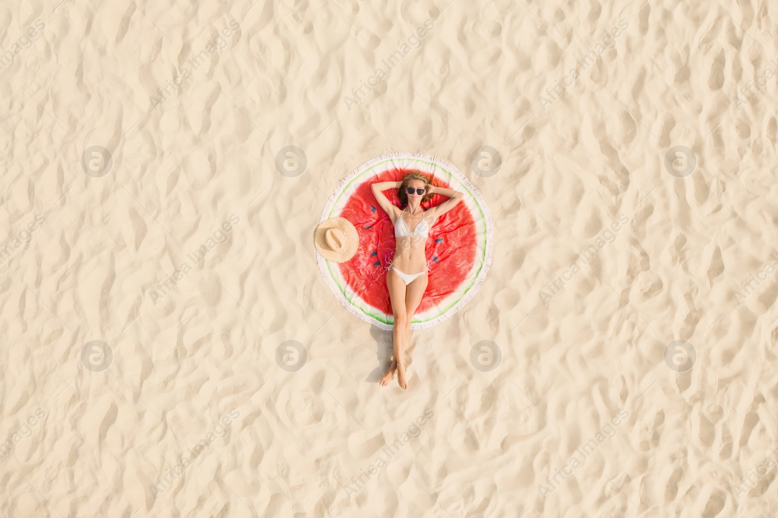 Image of Woman sunbathing on round beach towel at sandy coast, aerial view