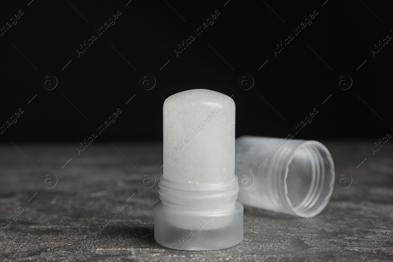 Photo of Natural crystal alum deodorant and cap on grey table against black background