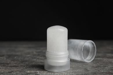 Natural crystal alum deodorant and cap on grey table against black background