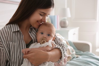 Happy mother holding her cute little baby with pacifier at home, space for text