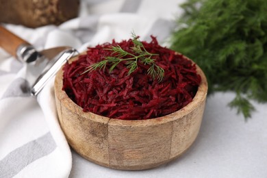 Grated red beet and dill in wooden bowl on table, closeup