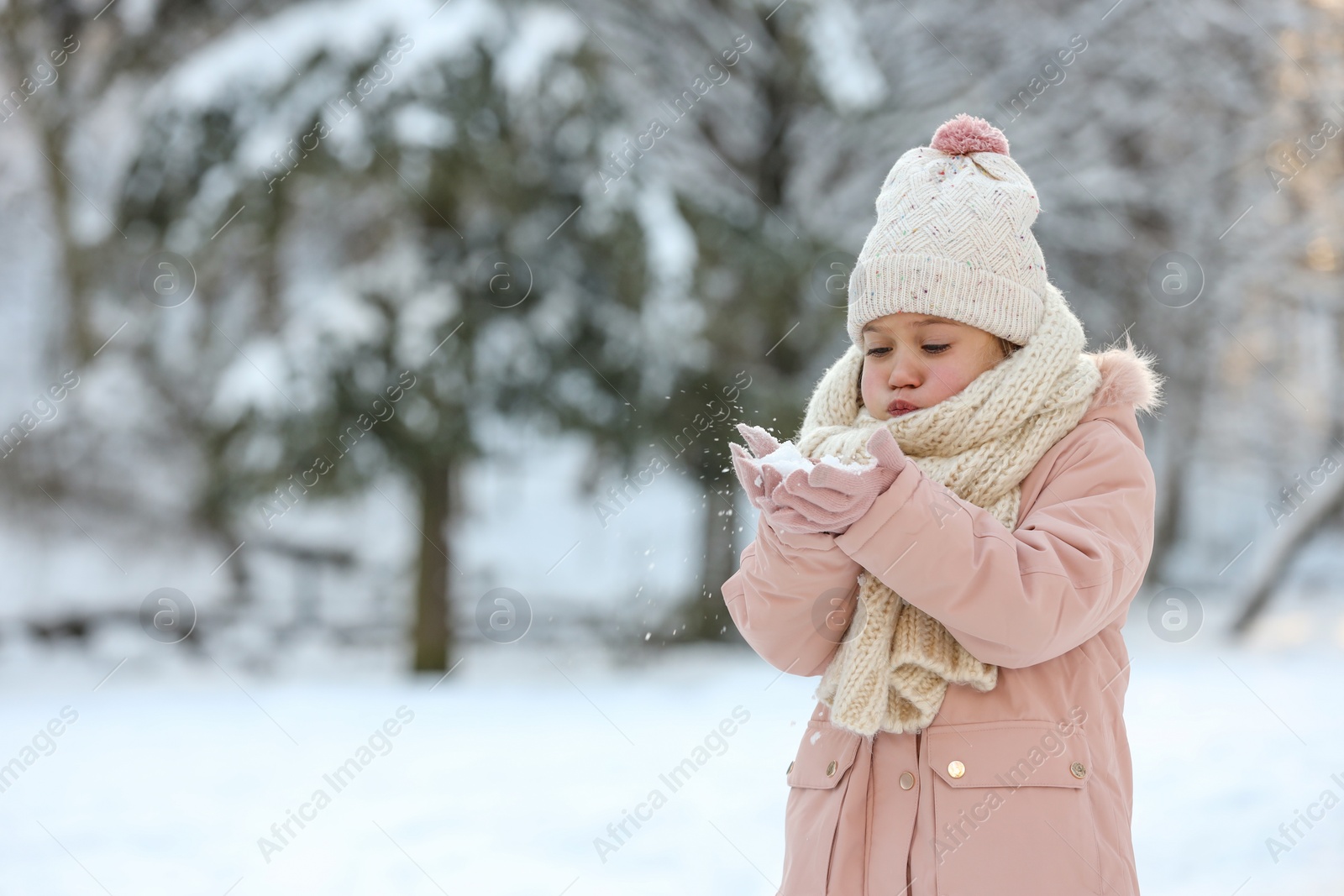 Photo of Cute little girl blowing snow in park on winter day, space for text