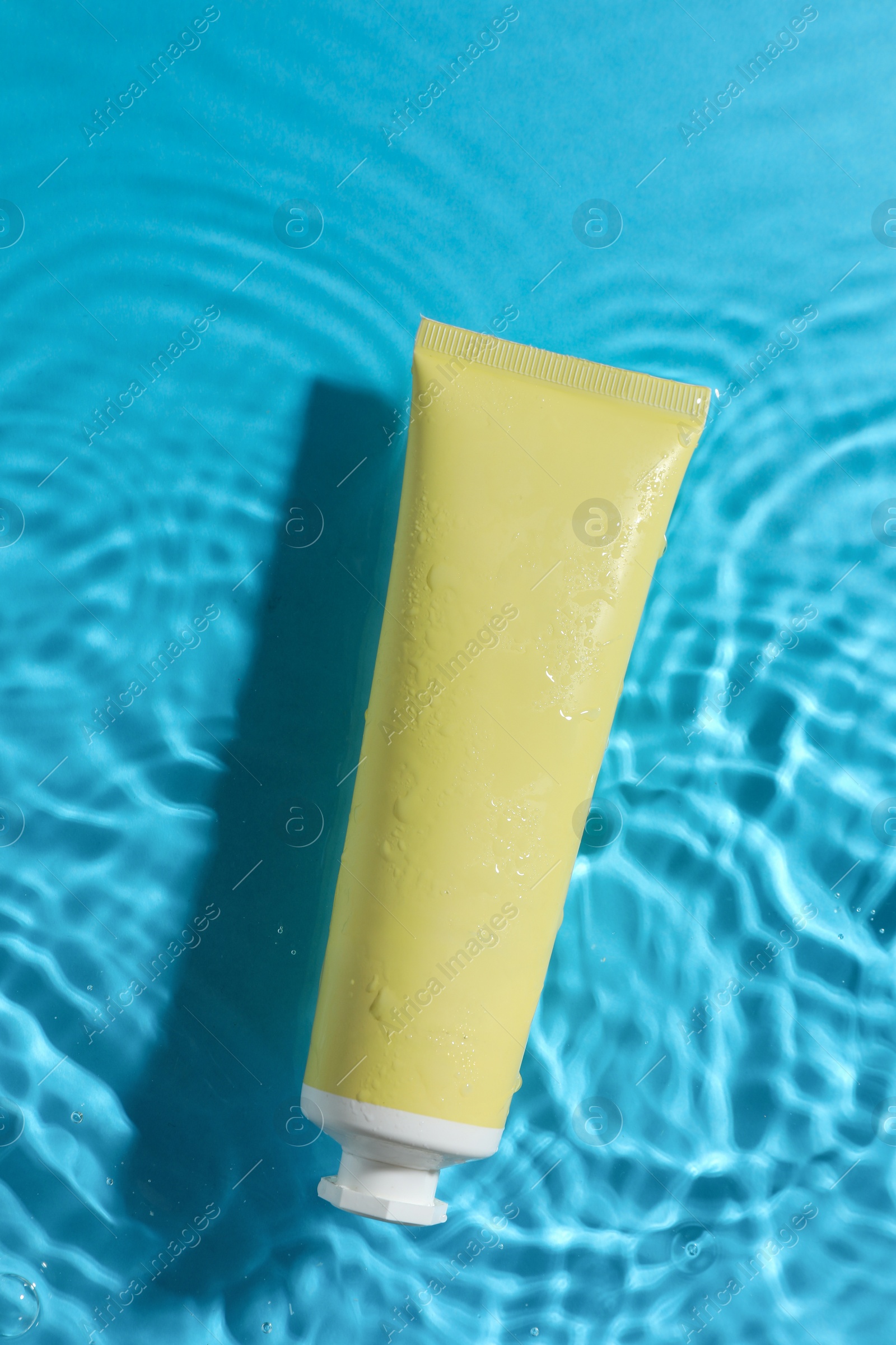 Photo of Tube with moisturizing cream in water on light blue background, top view