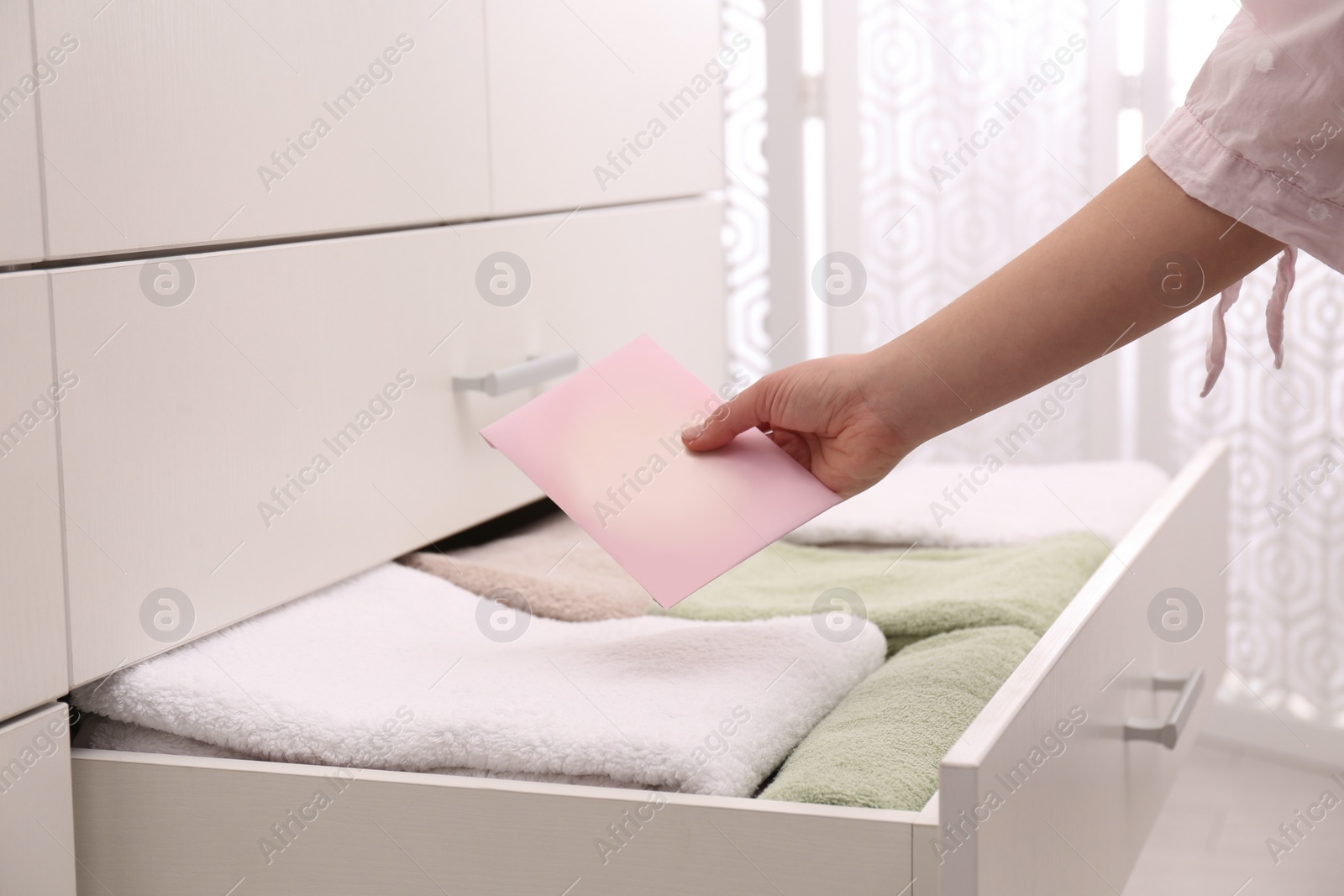 Photo of Woman putting scented sachet into drawer with towels, closeup