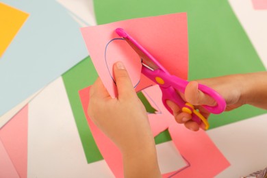 Little girl cutting color paper with scissors at table, closeup