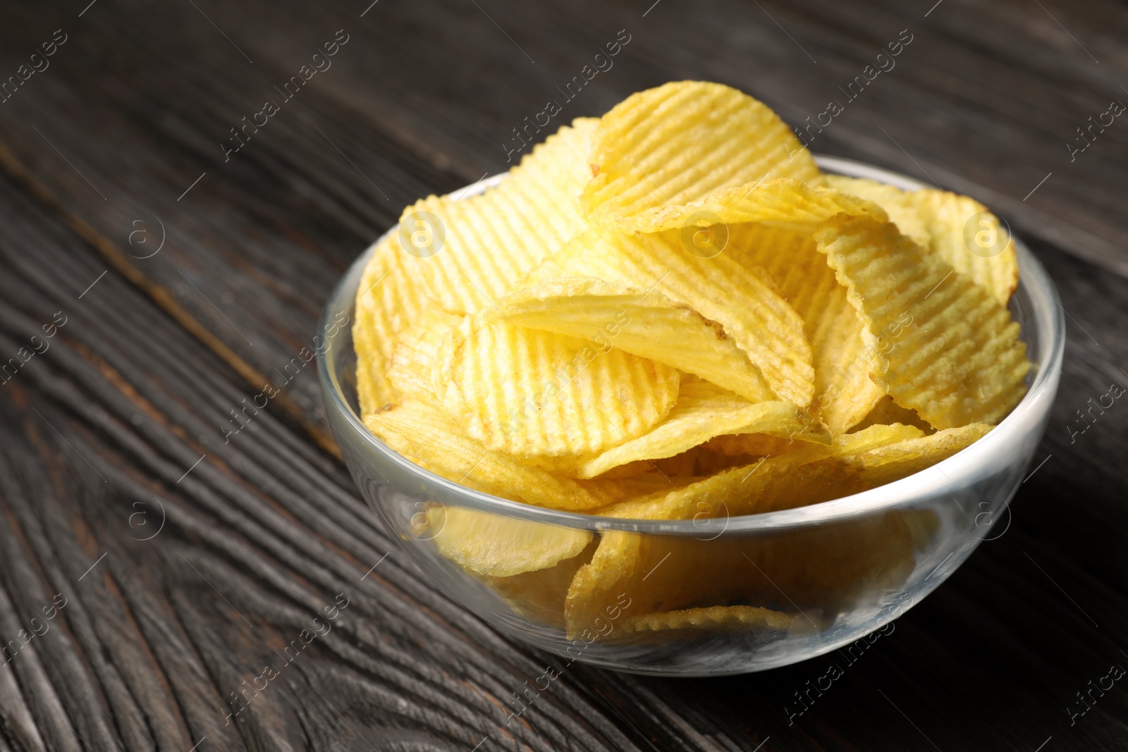 Photo of Bowl of potato chips on wooden table, closeup. Space for text