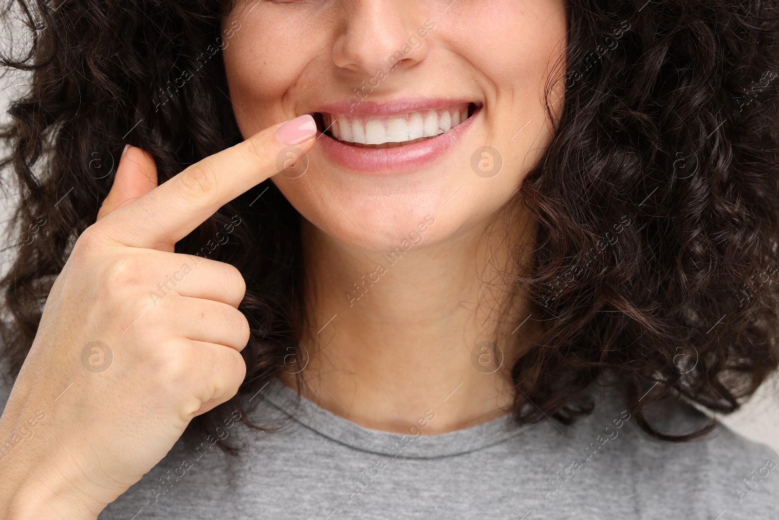 Photo of Young woman showing her teeth with whitening strip on light grey background, closeup