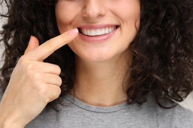 Photo of Young woman showing her teeth with whitening strip on light grey background, closeup