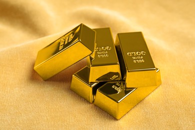 Photo of Many shiny gold bars on yellow fabric, closeup