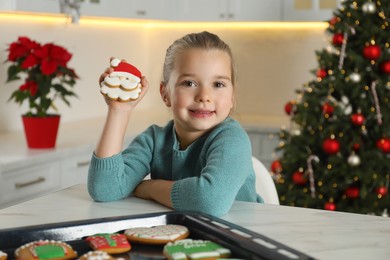 Photo of Cute little girl with freshly baked Christmas gingerbread cookie at table indoors