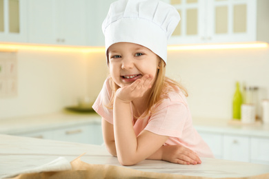 Photo of Portrait of cute little girl wearing chef hat in kitchen