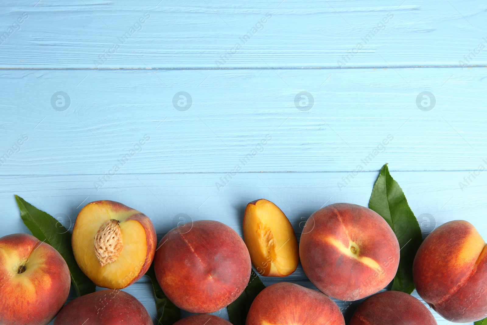 Photo of Fresh peaches and leaves on blue wooden table, top view with space for text