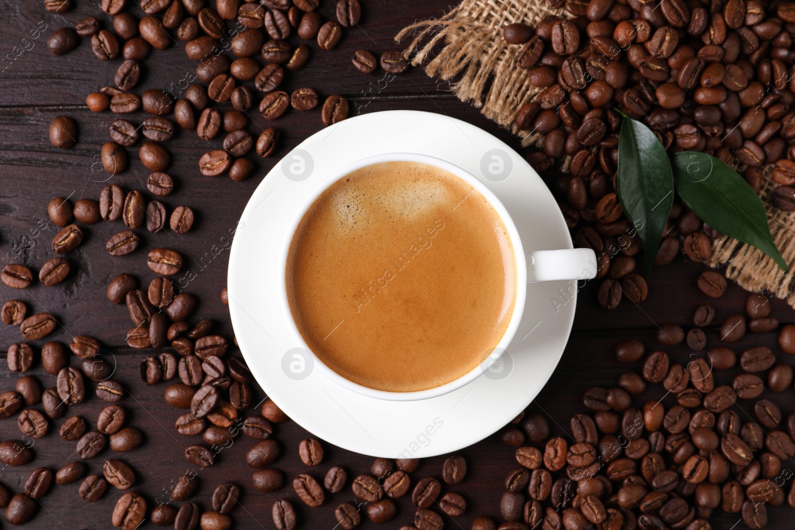 Photo of Cup of hot aromatic coffee and roasted beans on wooden table, flat lay