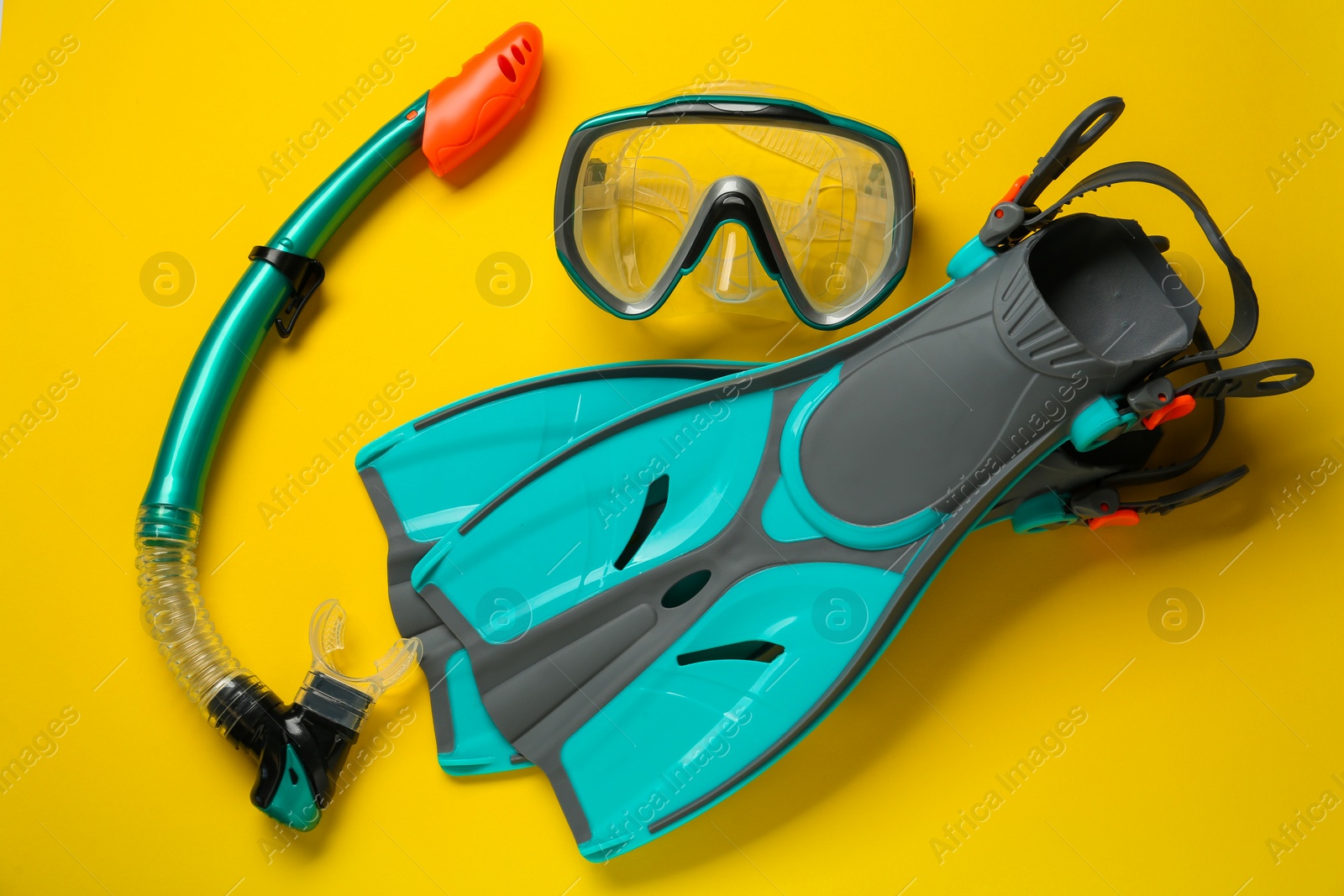 Photo of Pair of turquoise flippers and mask on yellow background, flat lay