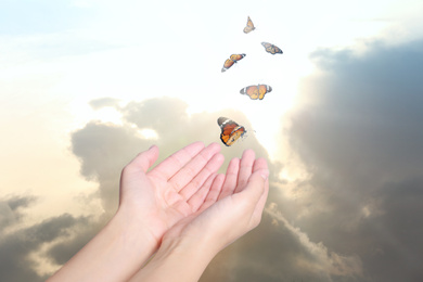 Image of Woman releasing butterflies against beautiful sky outdoors, closeup. Freedom concept
