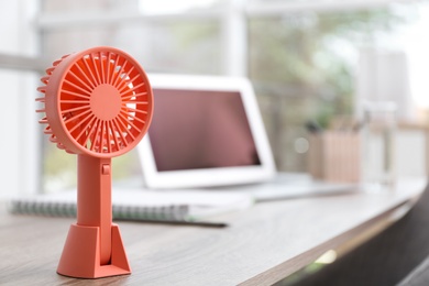 Modern portable fan on wooden table in office, space for text. Summer heat